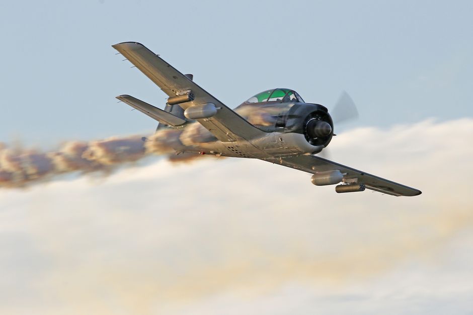 A gray military-style aircraft flying with smoke trails
