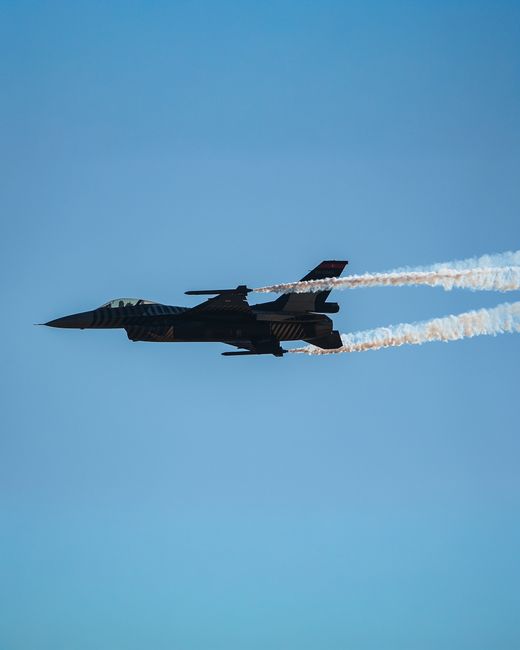 A fighter jet flying with contrails against a blue sky