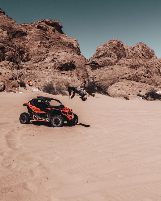 An orange and black ATV parked on sand with rocky formations in the background