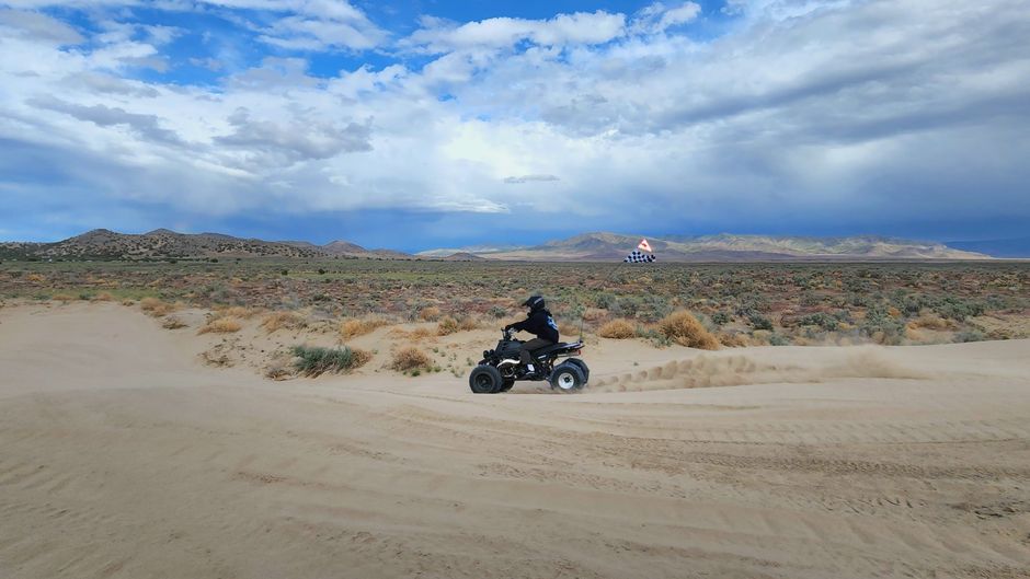 ATV on sandy terrain with desert landscape and American flag in distance
