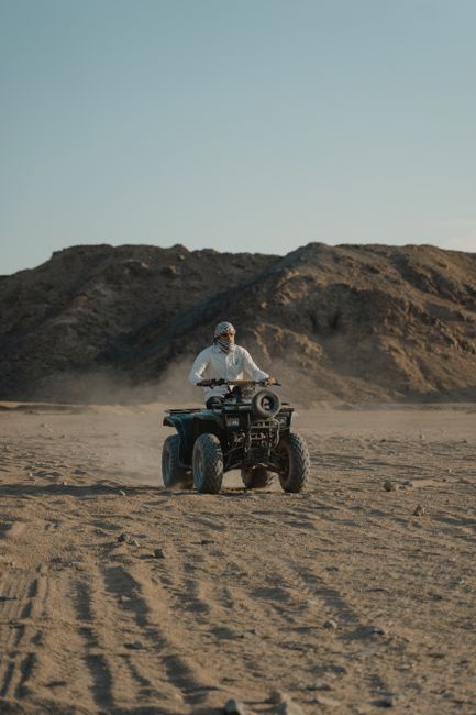 Person riding ATV on sandy terrain with large dunes in background