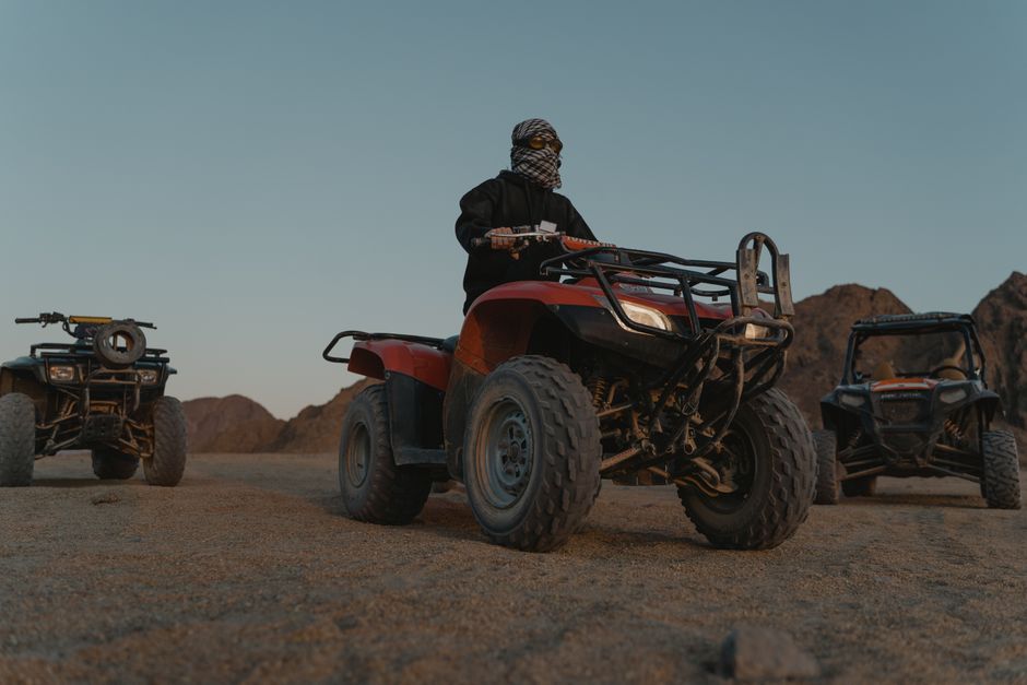 Person on red ATV with two other ATVs in desert landscape