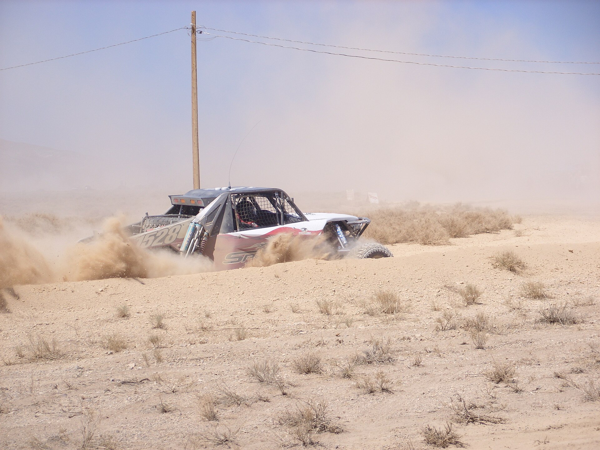 A red and white off-road vehicle kicking up dust on a dirt track