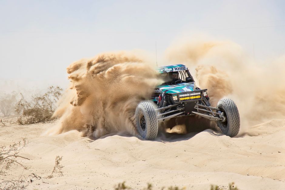 A green desert buggy kicking up sand on a dirt track
