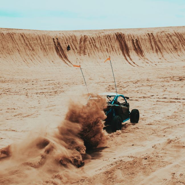 A blue desert buggy kicking up sand on a dirt track