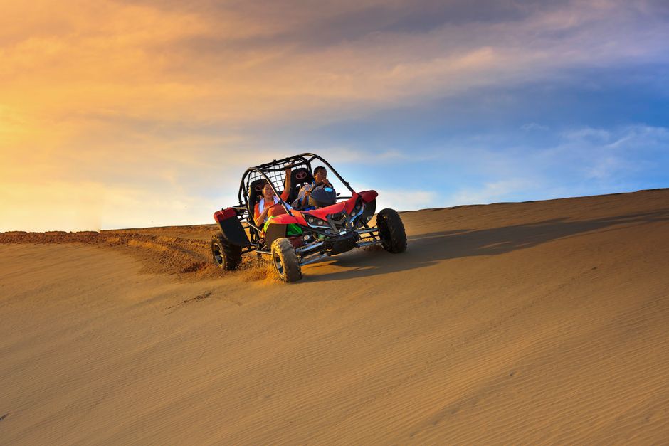 A red desert buggy with two people driving on sand dunes