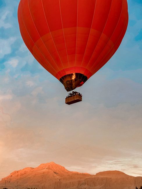 A red hot air balloon flying over mountains at sunrise