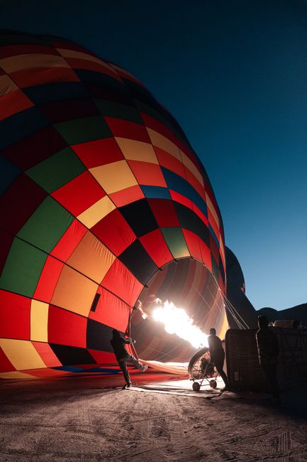 A large multicolored hot air balloon being inflated on the ground with people nearby