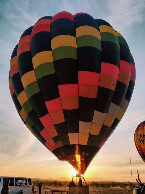 A large hot air balloon with a multicolored checkered pattern on the ground at sunrise