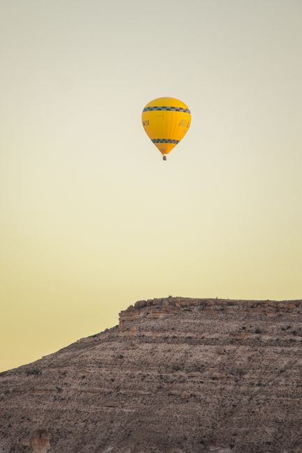 A yellow hot air balloon flying over a desert hill at sunrise