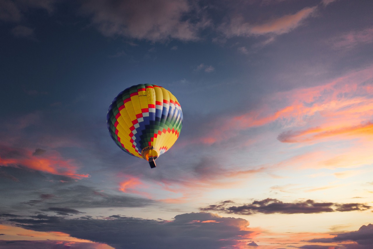 A colorful hot air balloon flying in a blue sky with pink and orange clouds