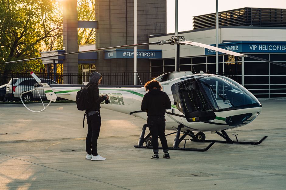 Two people standing next to a white and green helicopter on a helipad