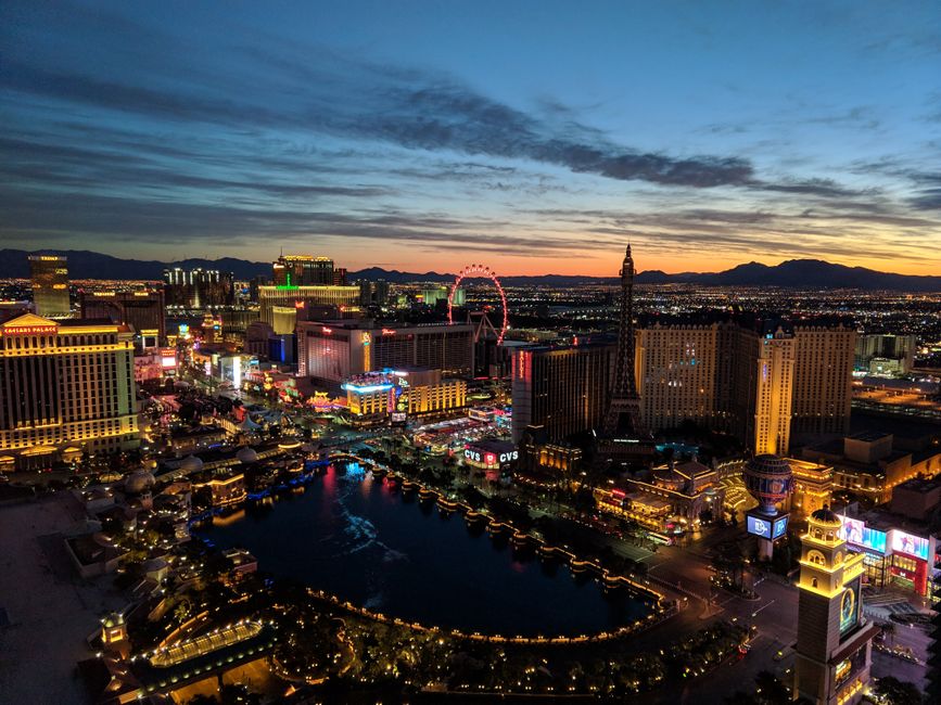 Aerial view of the Las Vegas Strip at dusk with lit buildings and a large pool in the foreground