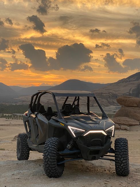 Off-road UTV vehicle parked on a dirt path with a desert landscape and sunset in the background