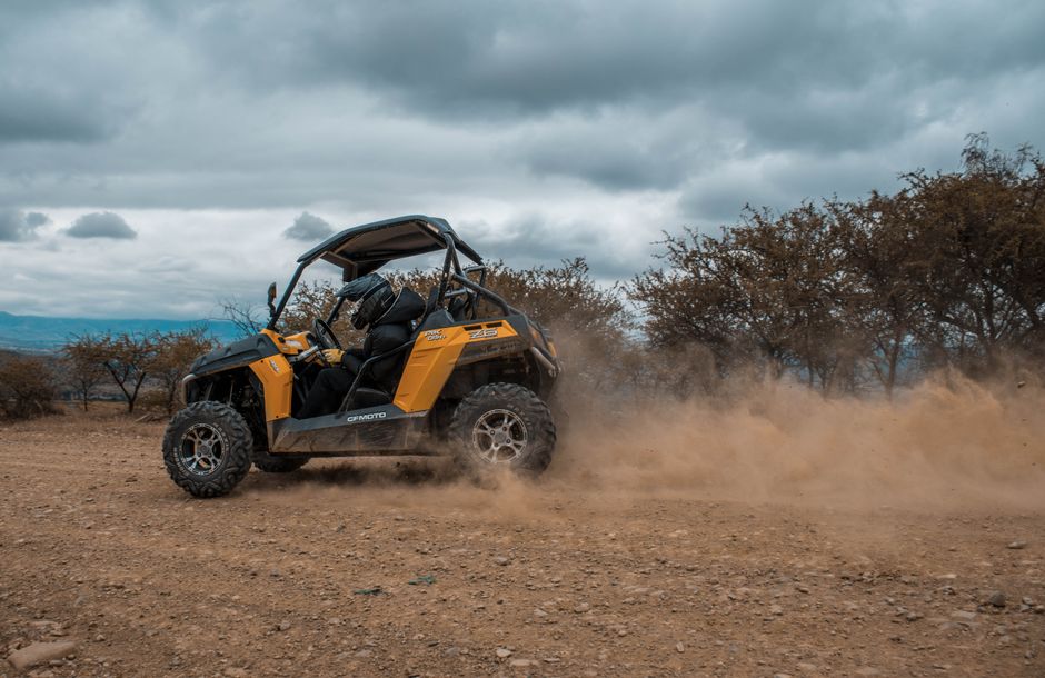 An orange and black UTV driving on dirt, kicking up dust