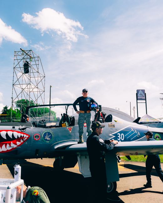 a gray stunt plane with a shark mouth painted on the nose and people standing around it