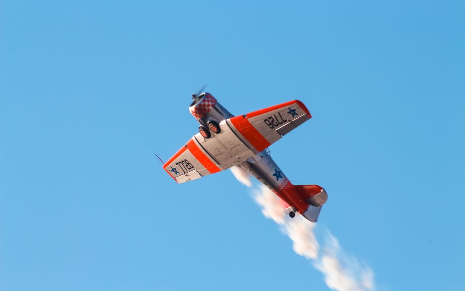 An orange and white stunt plane flying upside down with smoke trailing