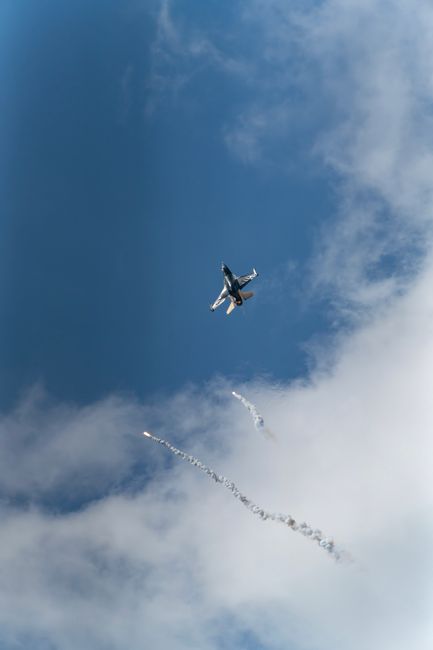 A small airplane flying in a blue sky with white clouds leaving behind smoke trails
