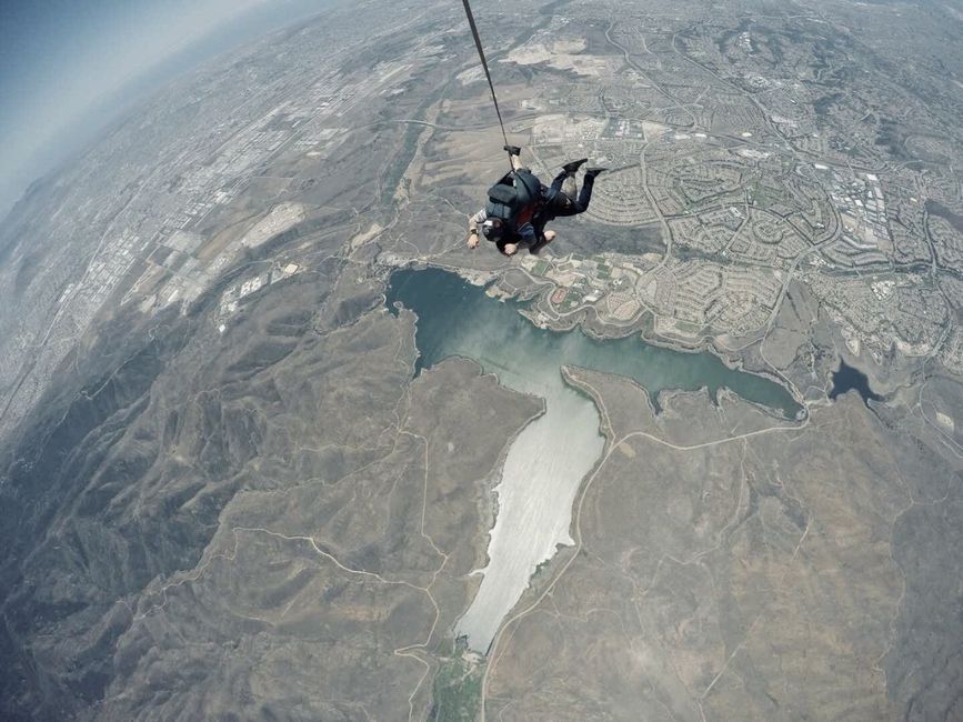 Two people skydiving over a landscape with a large body of water