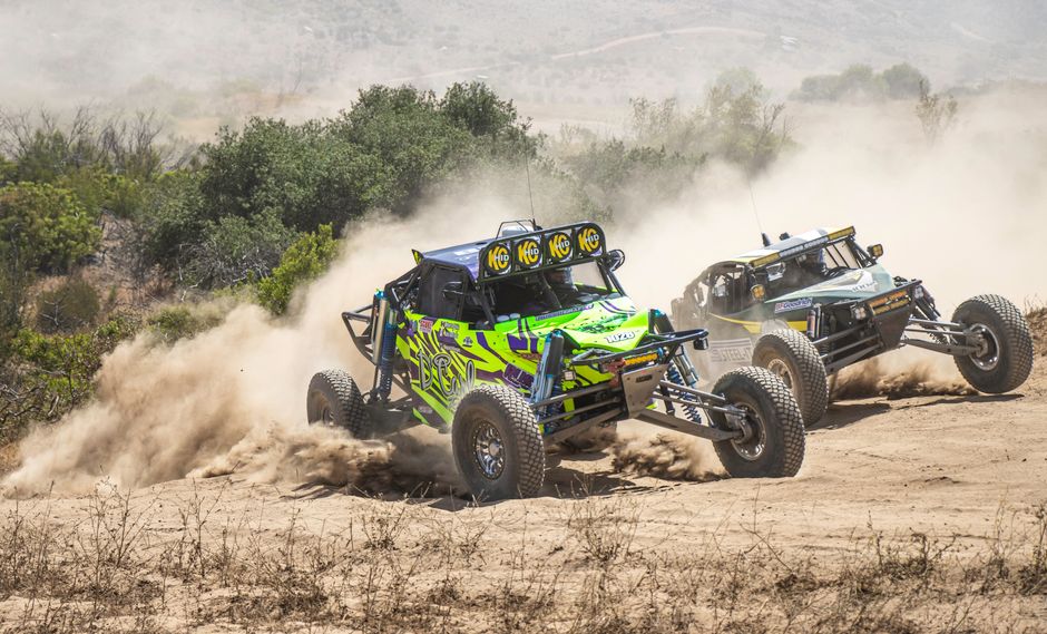 Two off-road vehicles racing on a dirt track, kicking up dust