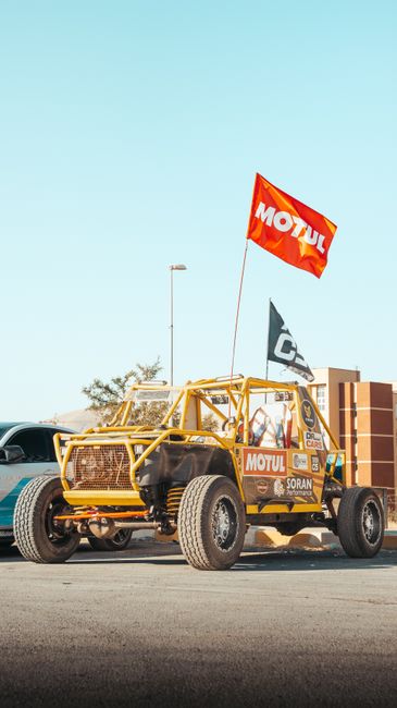 A yellow off-road vehicle with MOTUL branding and flags, parked on asphalt