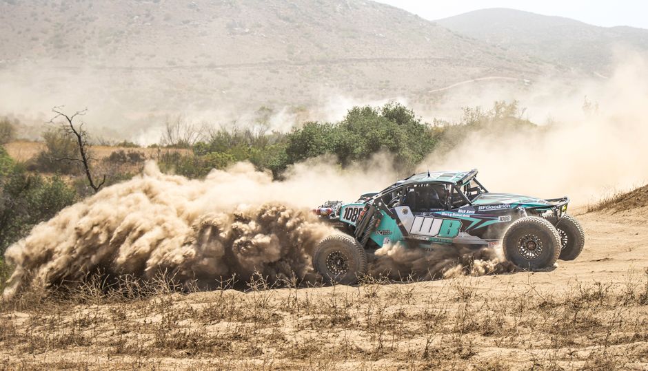 A teal off-road vehicle kicking up dust on a dirt track